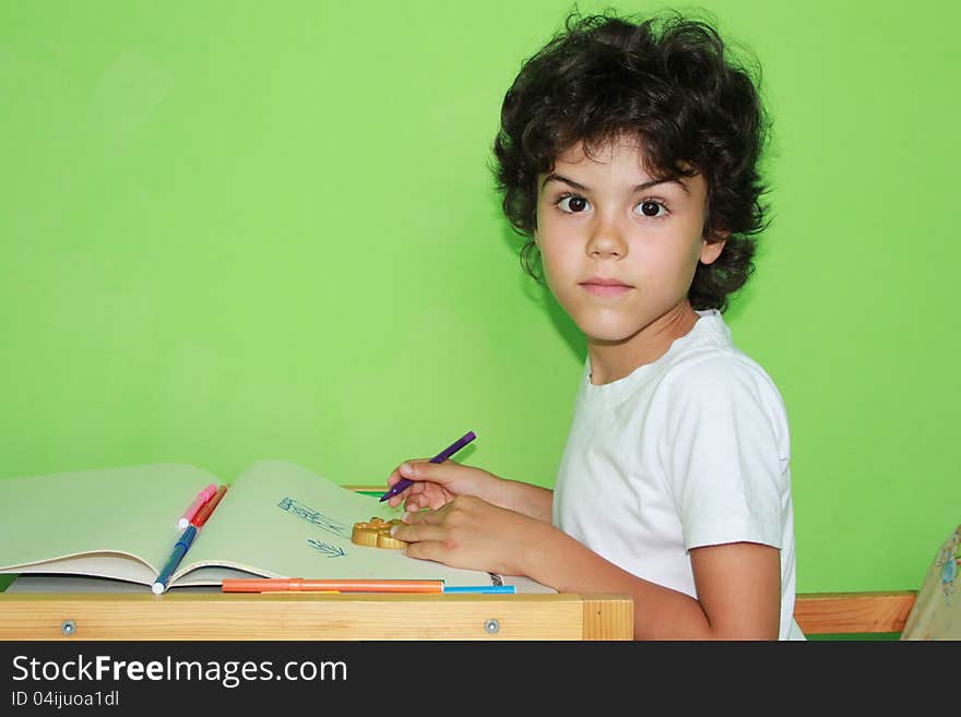 Little curly boy is drawing with colored pencils at home