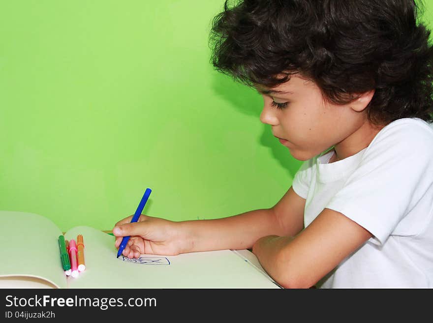 Little curly boy is drawing with colored pencils at home