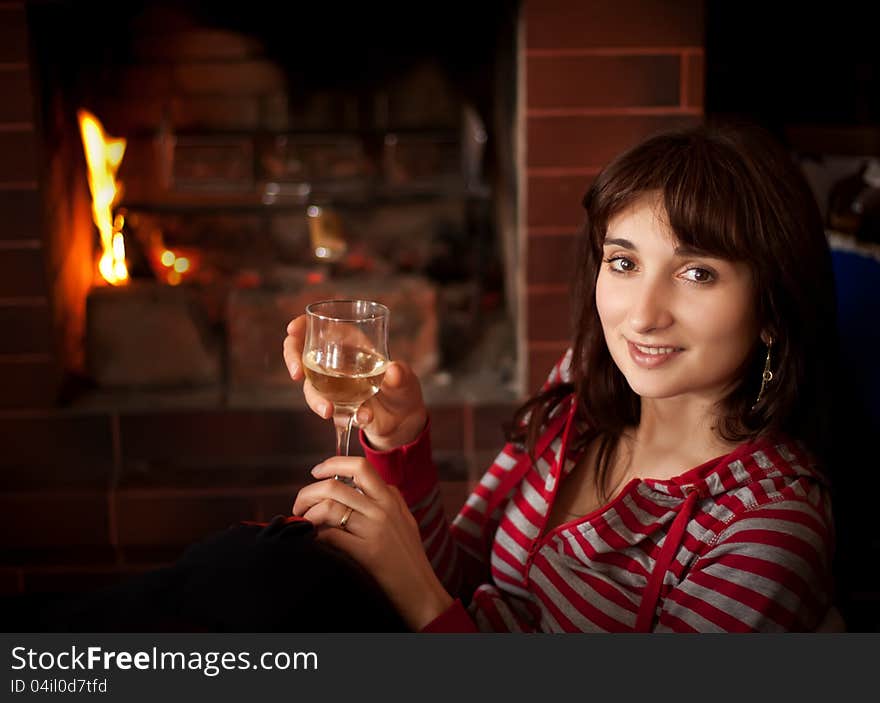 Portrait of a young woman with a glass of wine near the fireplace