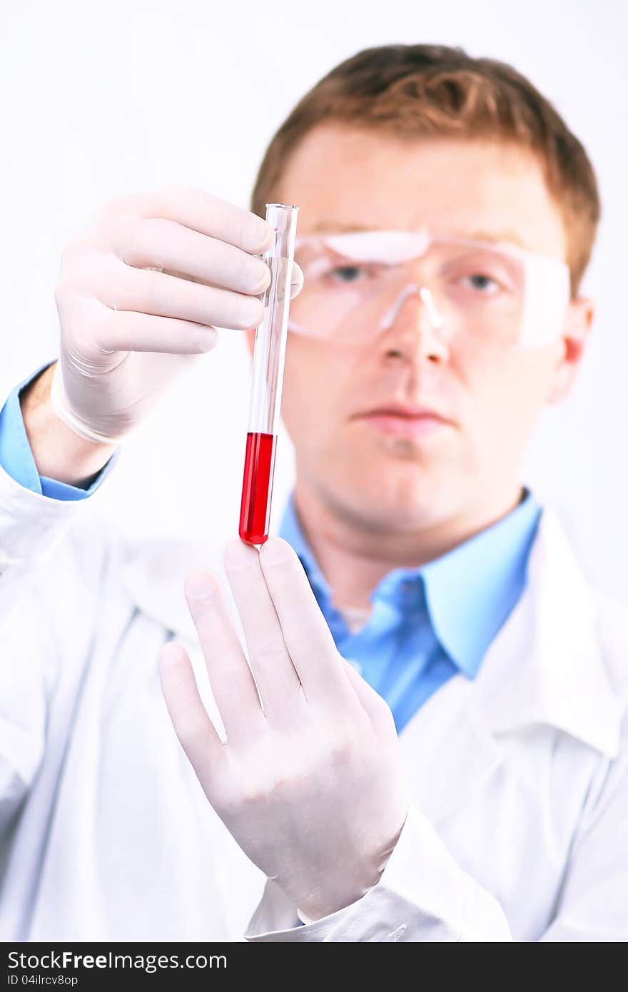 Man in white coat and protective glasses looking at a sample of red liquid test tube. Man in white coat and protective glasses looking at a sample of red liquid test tube