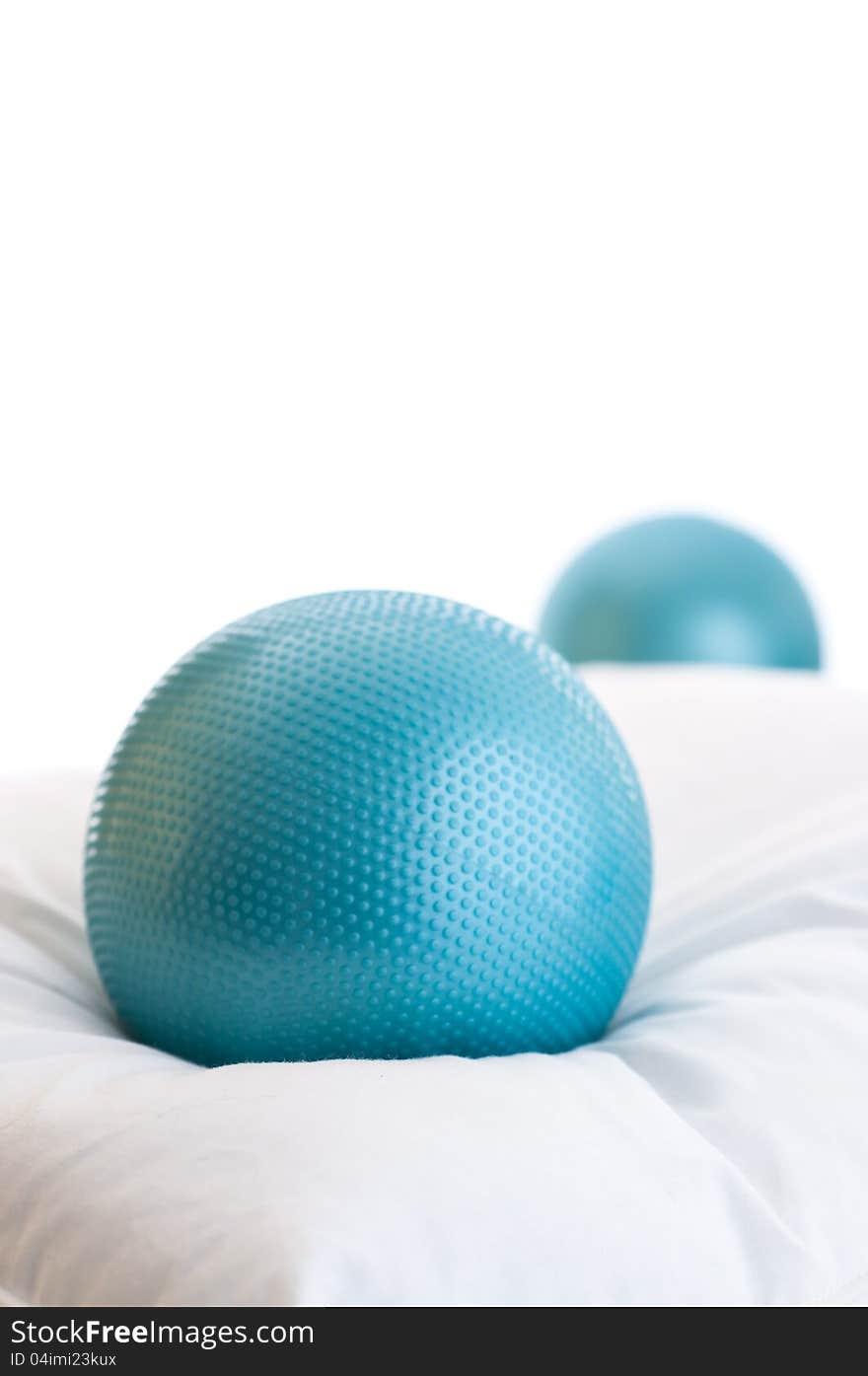 One blue exercise ball resting on pillow with a second ball in background, with plenty of white copy space. One blue exercise ball resting on pillow with a second ball in background, with plenty of white copy space