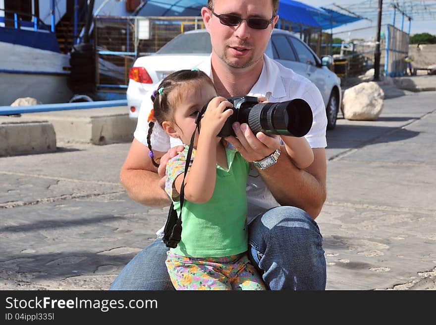 Dad teaches his daughter to photograph their camera, and maintains its bottom. Dad teaches his daughter to photograph their camera, and maintains its bottom