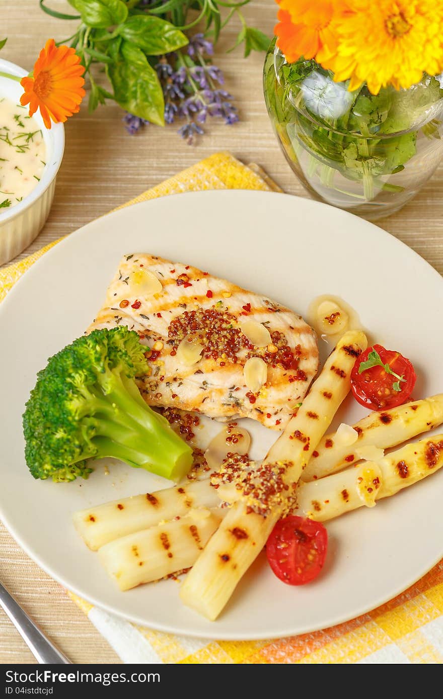 Grilled chicken breast with asparagus, broccoli, and spring tomatoes on white plate. Grilled chicken breast with asparagus, broccoli, and spring tomatoes on white plate