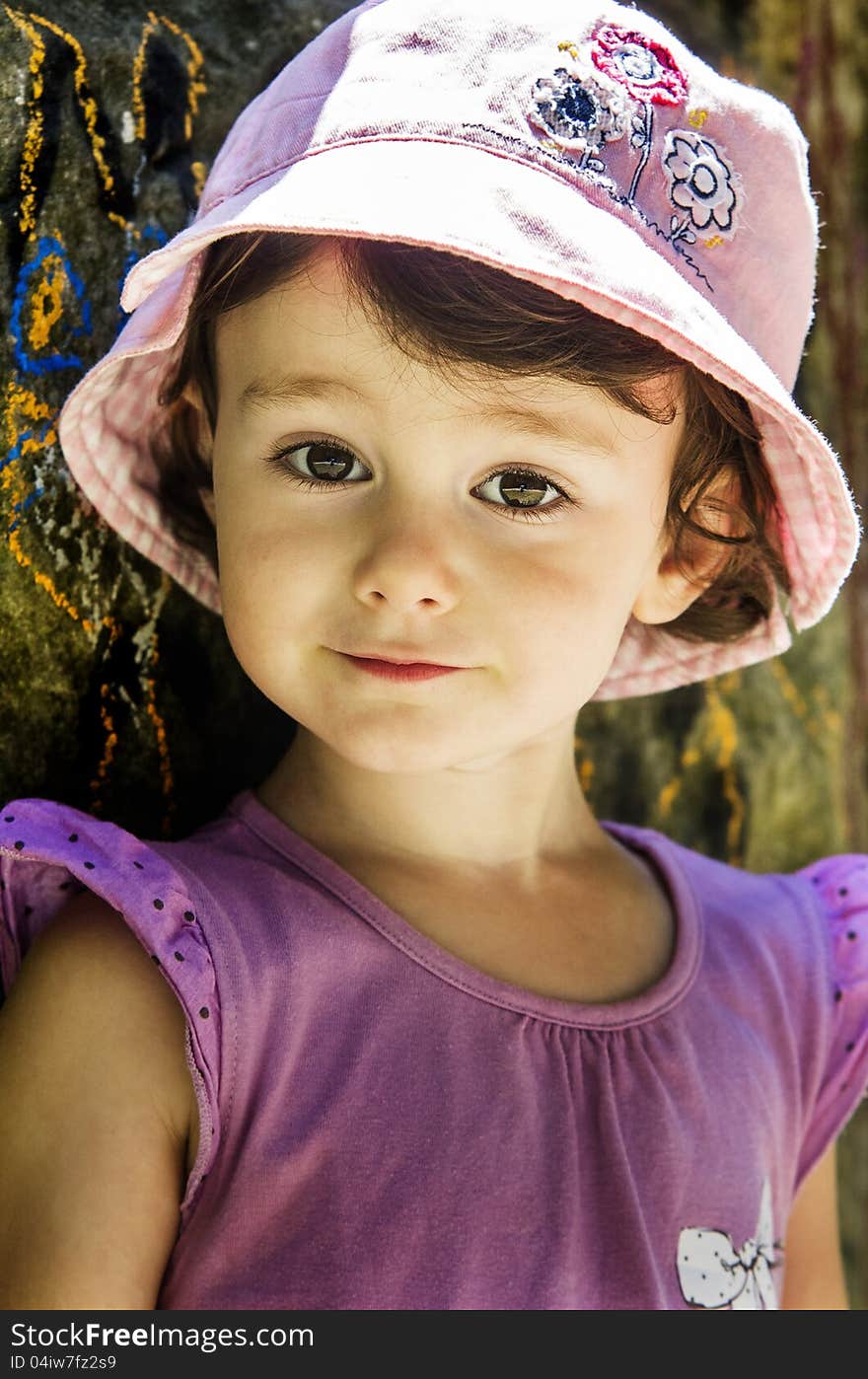 Small girl in pink hat leaning against a wall