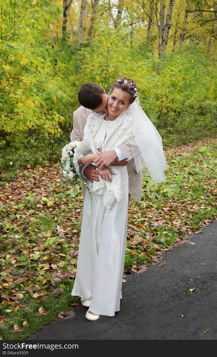 Young groom hugs his bride and kisses neck