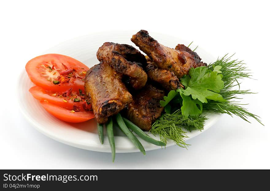 Barbecued pork ribs with tomato and greens on plate isolated on white background. Barbecued pork ribs with tomato and greens on plate isolated on white background