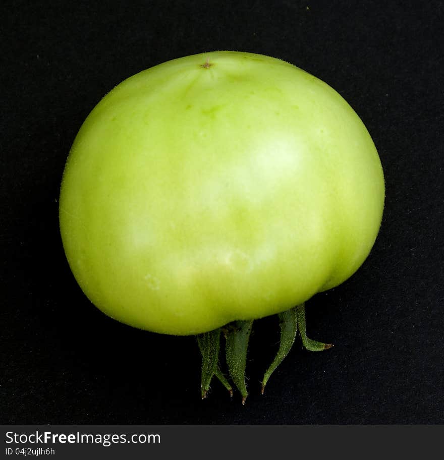 Green, raw tomato on black platform. Green, raw tomato on black platform.