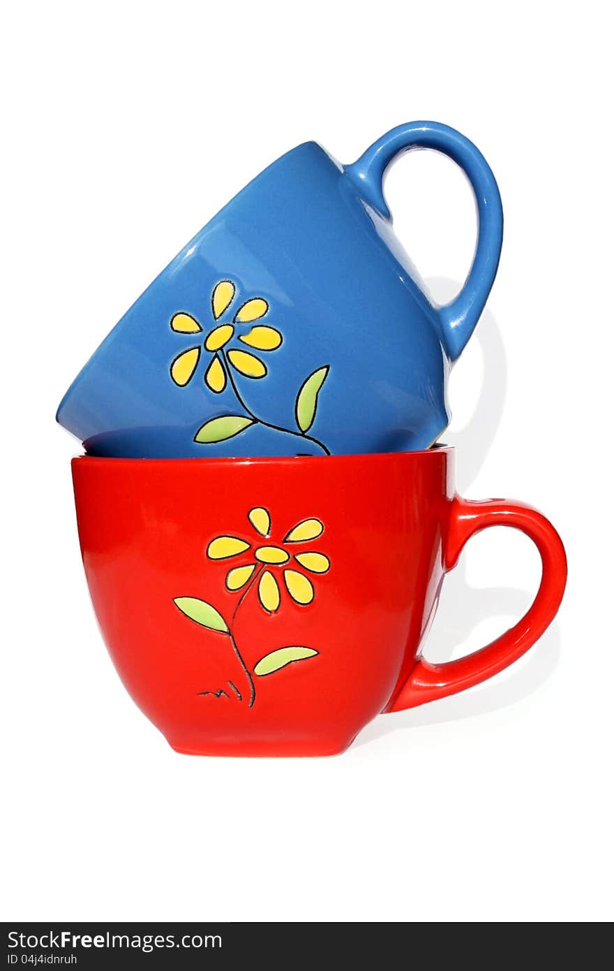 Red and dark blue mugs with yellow flower on white background. Photo.