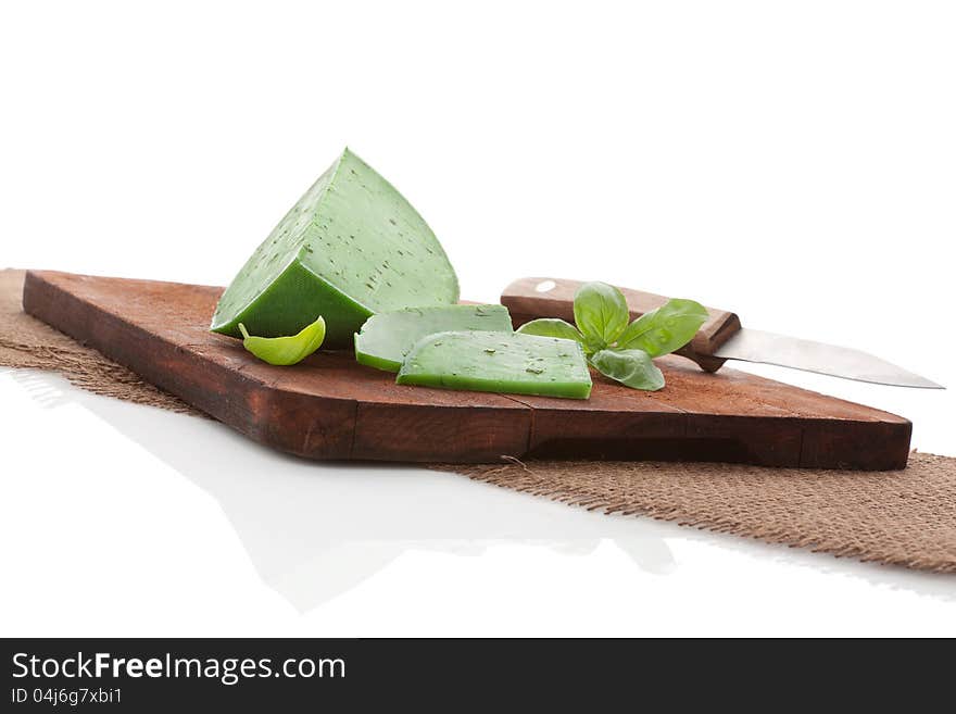 Green cheese gouda with pesto on dark brown chopping board with fresh basil leaf and knife. Minimal cheese still life. Green cheese gouda with pesto on dark brown chopping board with fresh basil leaf and knife. Minimal cheese still life.