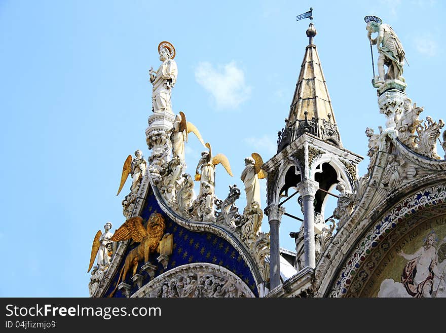 The richly decorated facade of a Venetian church features the emblem of the city: the winged lion holding a book, as well as a group of golden winged angels paying homage to a saint. The richly decorated facade of a Venetian church features the emblem of the city: the winged lion holding a book, as well as a group of golden winged angels paying homage to a saint.