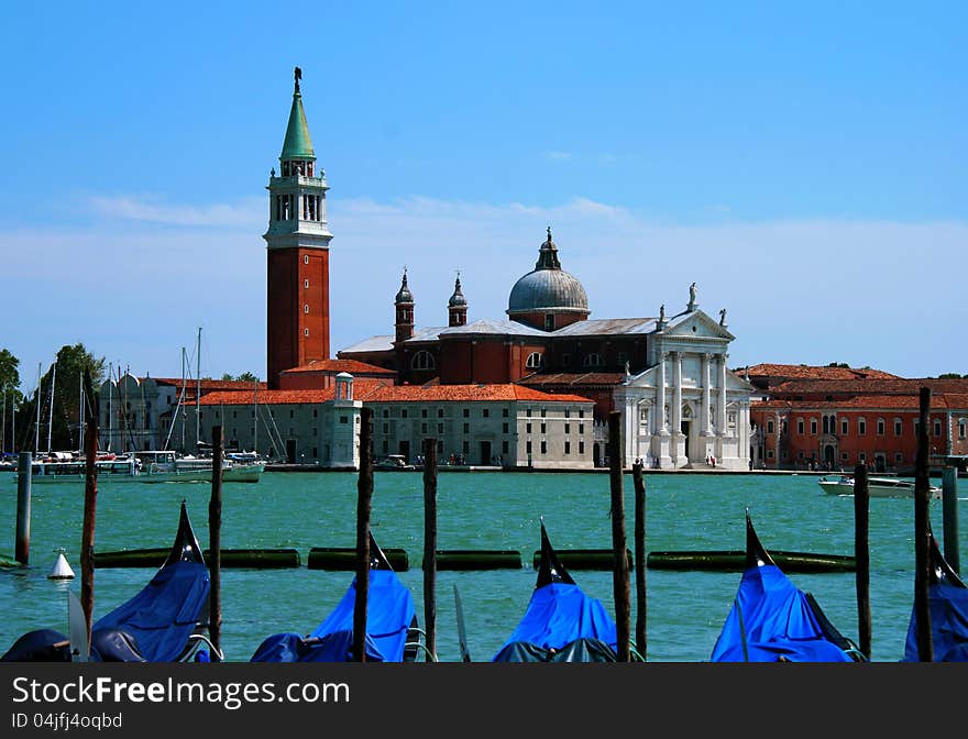 A fetching view across the sea towards the San Giorgio Maggiore island in Venice, Italy. In the foreground a row of traditional gondolas anchored in their pier.