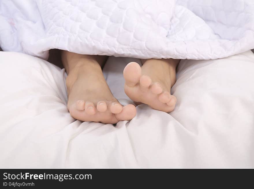 Feet of a woman sleeping on the white bed on the bedroom. Feet of a woman sleeping on the white bed on the bedroom