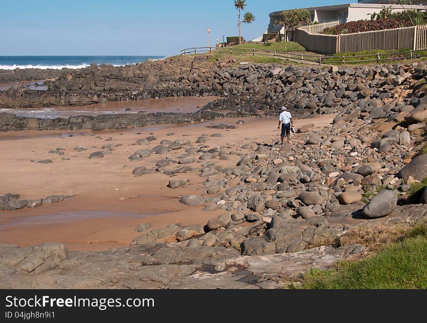 An African man picks his way across boulders on a beach at Ballito, KwaZulu-Natal North Coast, South Africa. An African man picks his way across boulders on a beach at Ballito, KwaZulu-Natal North Coast, South Africa.