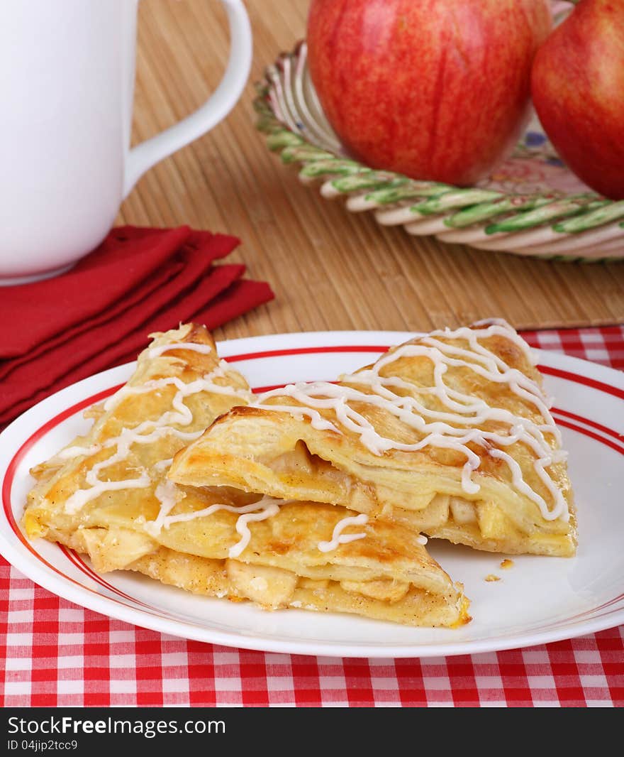 Two apple turnovers on a plate with apples in background