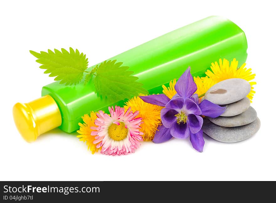 A green cosmetic bottle with nettle, dandelion, daisy, columbine and zen stones on a white background. A green cosmetic bottle with nettle, dandelion, daisy, columbine and zen stones on a white background