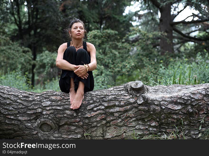 Portrait of strength attractive mature woman in black sitting on wooden log in forest. Portrait of strength attractive mature woman in black sitting on wooden log in forest