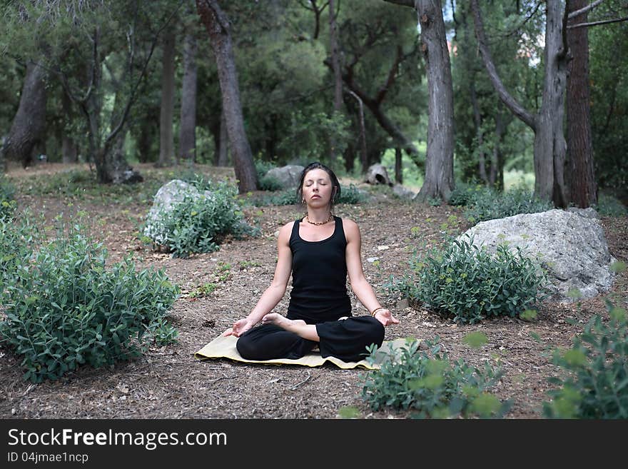 Svelte adult woman in black sitting in lotus position on forest background. Svelte adult woman in black sitting in lotus position on forest background