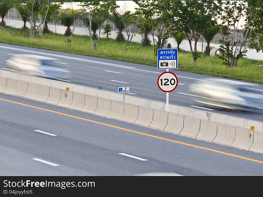 Speed limit (120 km/hour) and speed camera signpost on motor way with cars in motion. Speed limit (120 km/hour) and speed camera signpost on motor way with cars in motion