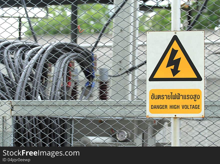 High voltage transformer substation behind barbed wire chain link fence with Danger High Voltage sign.