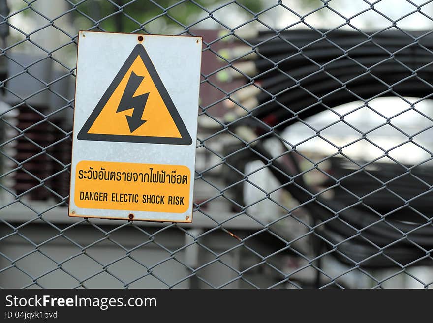 High voltage transformer substation behind barbed wire chain link fence with Danger High Voltage sign.