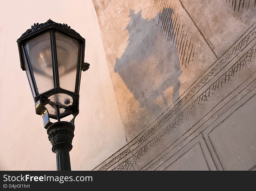 Details the top of the old metal lamp street lighting, lamp and her shadow on the wall