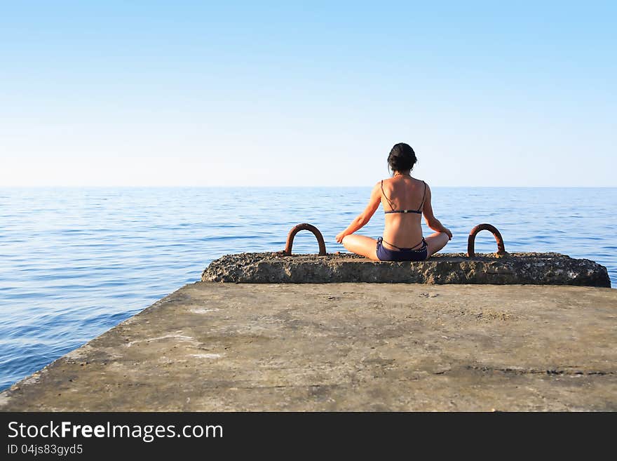 Svelte mature woman sitting on pier near sea and looking to horizon. Svelte mature woman sitting on pier near sea and looking to horizon