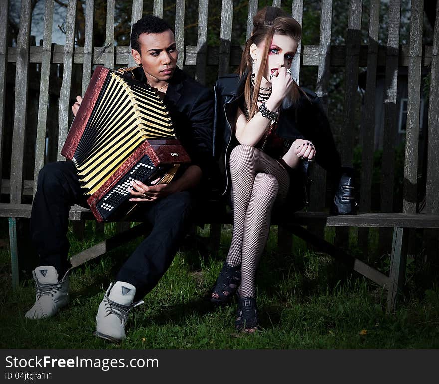 Couple young people - black men and white women sitting on bench against the fence. Accordion. Countryside. Serenade. Couple young people - black men and white women sitting on bench against the fence. Accordion. Countryside. Serenade