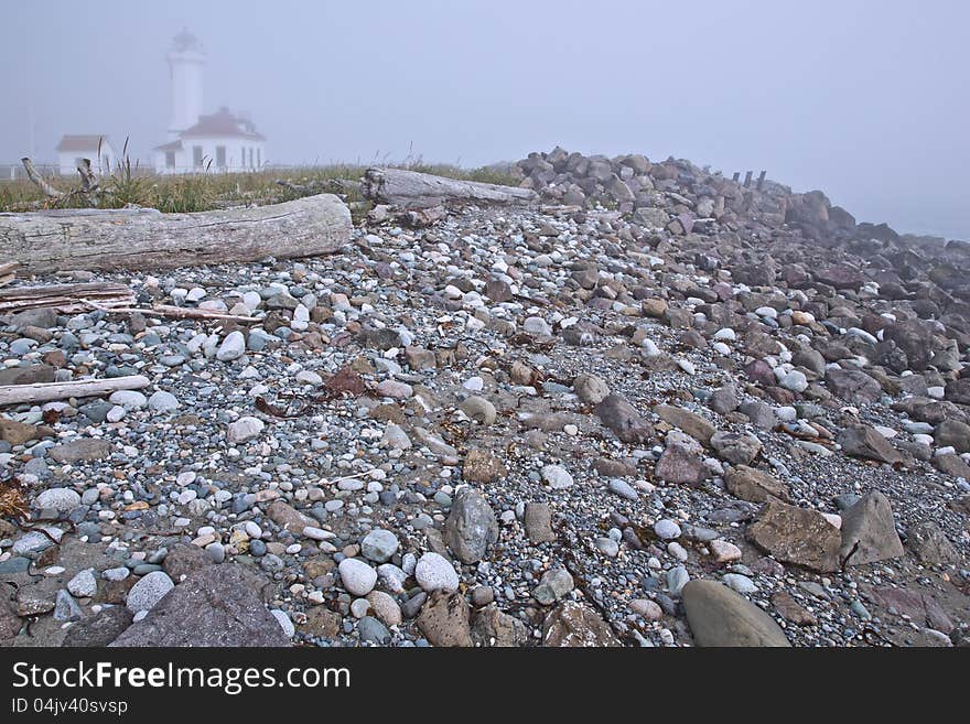 Thick morning fog surrounds the Point Wilson Lighthouse from the viewpoint of a classic Pacific Northwest rocky beach at the Fort Worden State Park. Thick morning fog surrounds the Point Wilson Lighthouse from the viewpoint of a classic Pacific Northwest rocky beach at the Fort Worden State Park