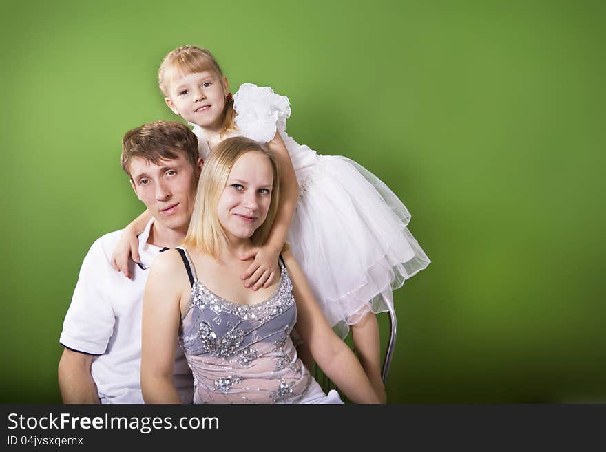 Young European family from three persons - mother, father and daughter. On a green background. Young European family from three persons - mother, father and daughter. On a green background.