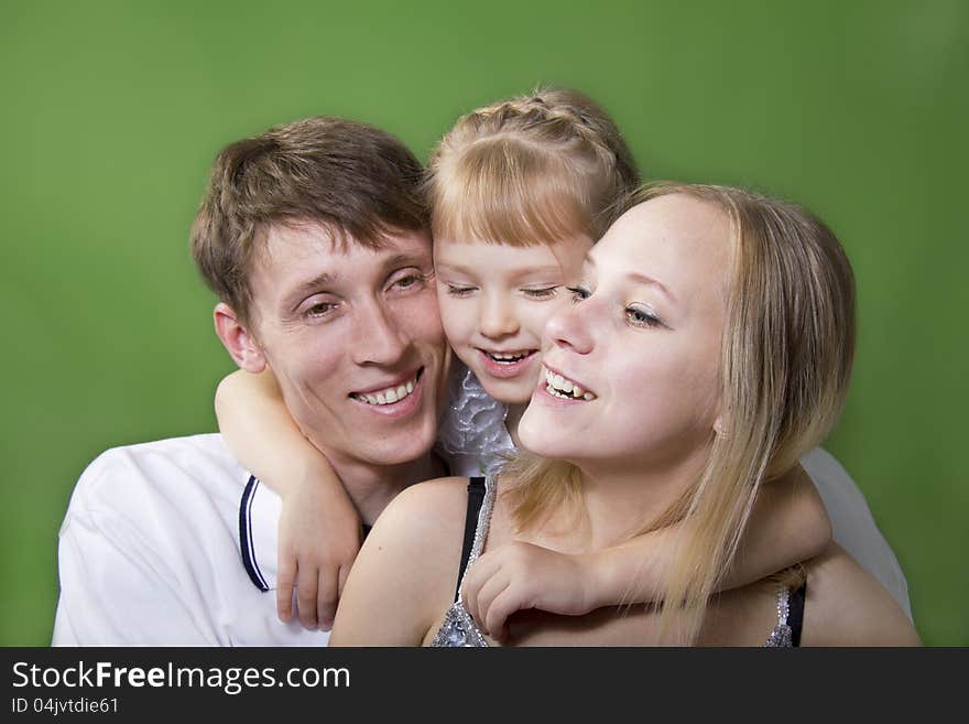 Young European family from three persons - mother, father and daughter. On a green background. Young European family from three persons - mother, father and daughter. On a green background.