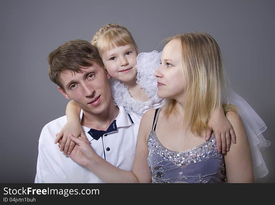 Young European family from three persons - mother, father and daughter. On a gray background. Young European family from three persons - mother, father and daughter. On a gray background