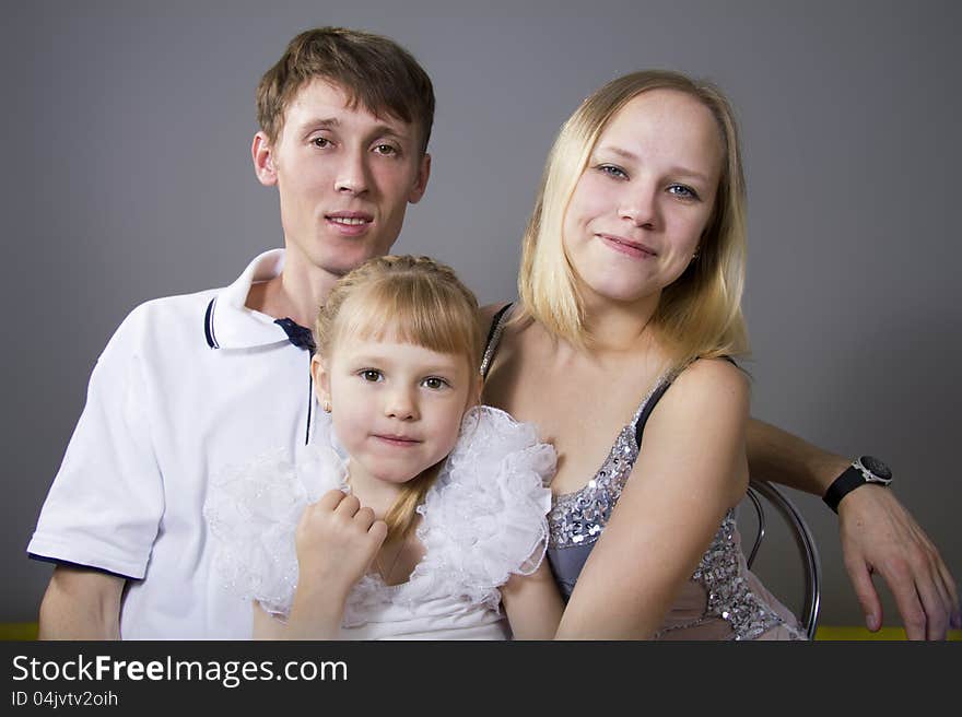 Young European family from three persons - mother, father and daughter. On a gray background. Young European family from three persons - mother, father and daughter. On a gray background