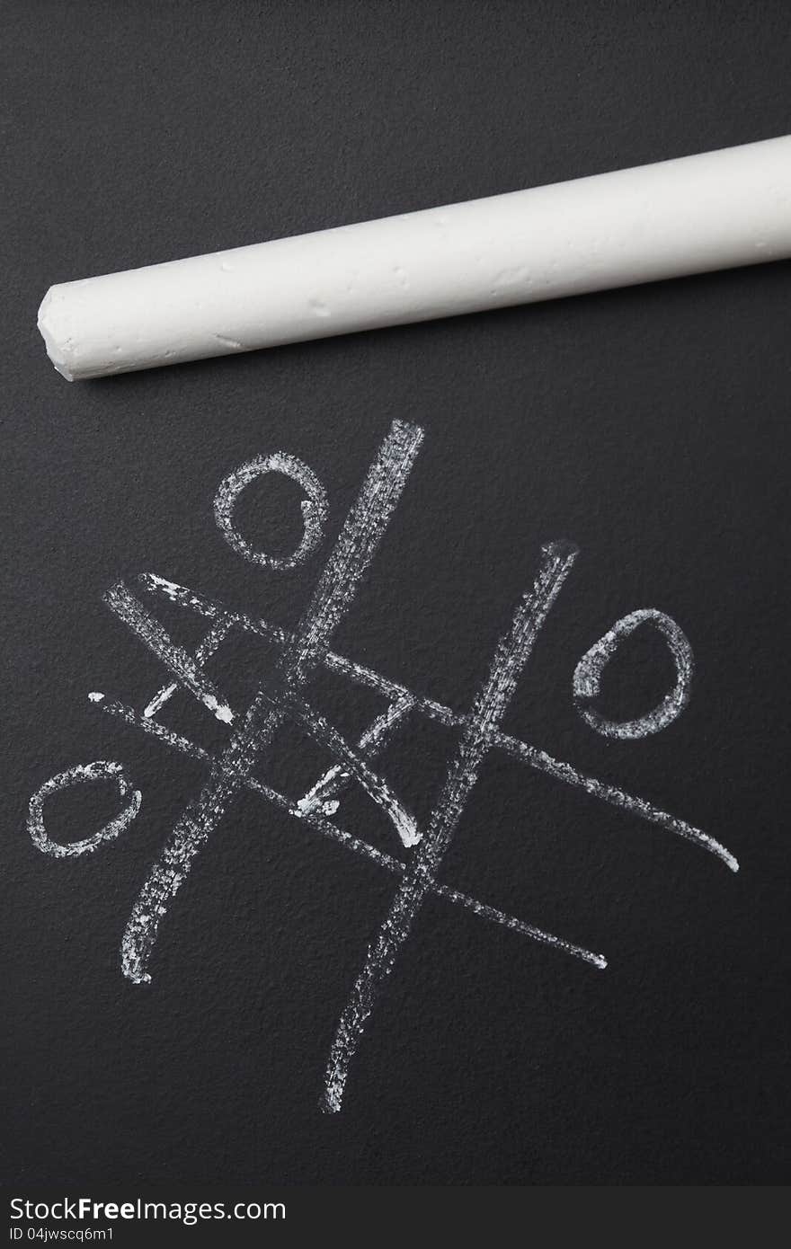 White chalk resting on black board with nought and crosses game. White chalk resting on black board with nought and crosses game