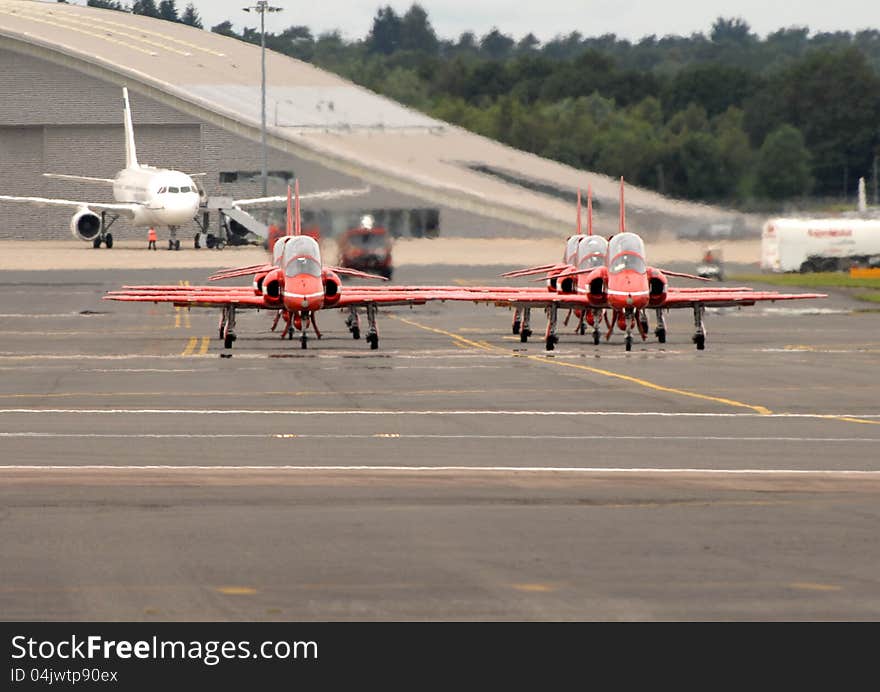 BAE Systems Hawk T1s of the RAF Red Arrows display team taxiing on the runway at Farnborough. England. Engine jet exhaust giving heat haze, with long lens compressed depth. BAE Systems Hawk T1s of the RAF Red Arrows display team taxiing on the runway at Farnborough. England. Engine jet exhaust giving heat haze, with long lens compressed depth.