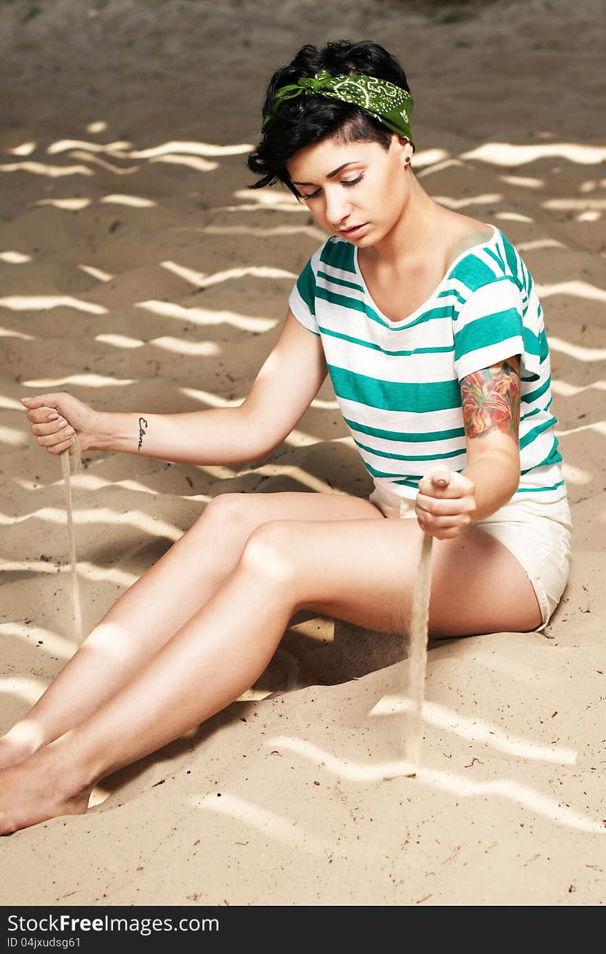 Girl with tattoo on the beach pours sand