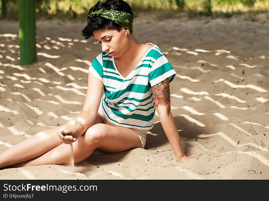 Girl with tattoo on the beach pours sand