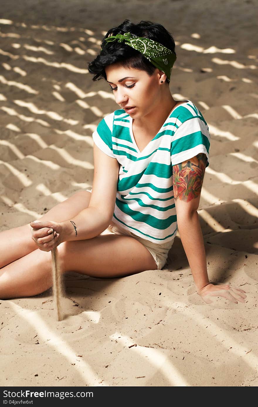 Girl with tattoo on the beach pours sand