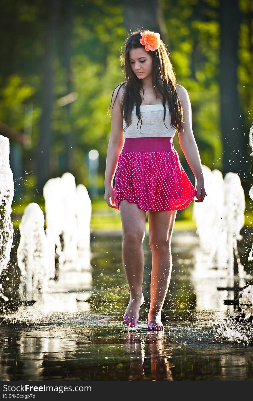 Young beautiful brunette girl wearing red skirt playing at outdoor water fountain in a hot day. Young beautiful brunette girl wearing red skirt playing at outdoor water fountain in a hot day