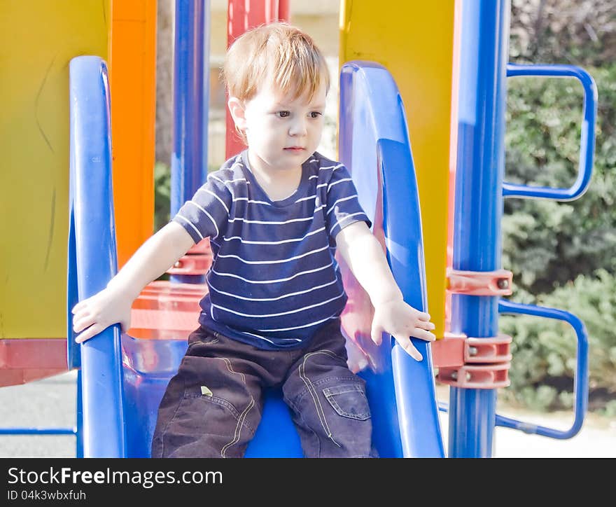 Small boy sitting on top the slide preparing to slide down. Small boy sitting on top the slide preparing to slide down.