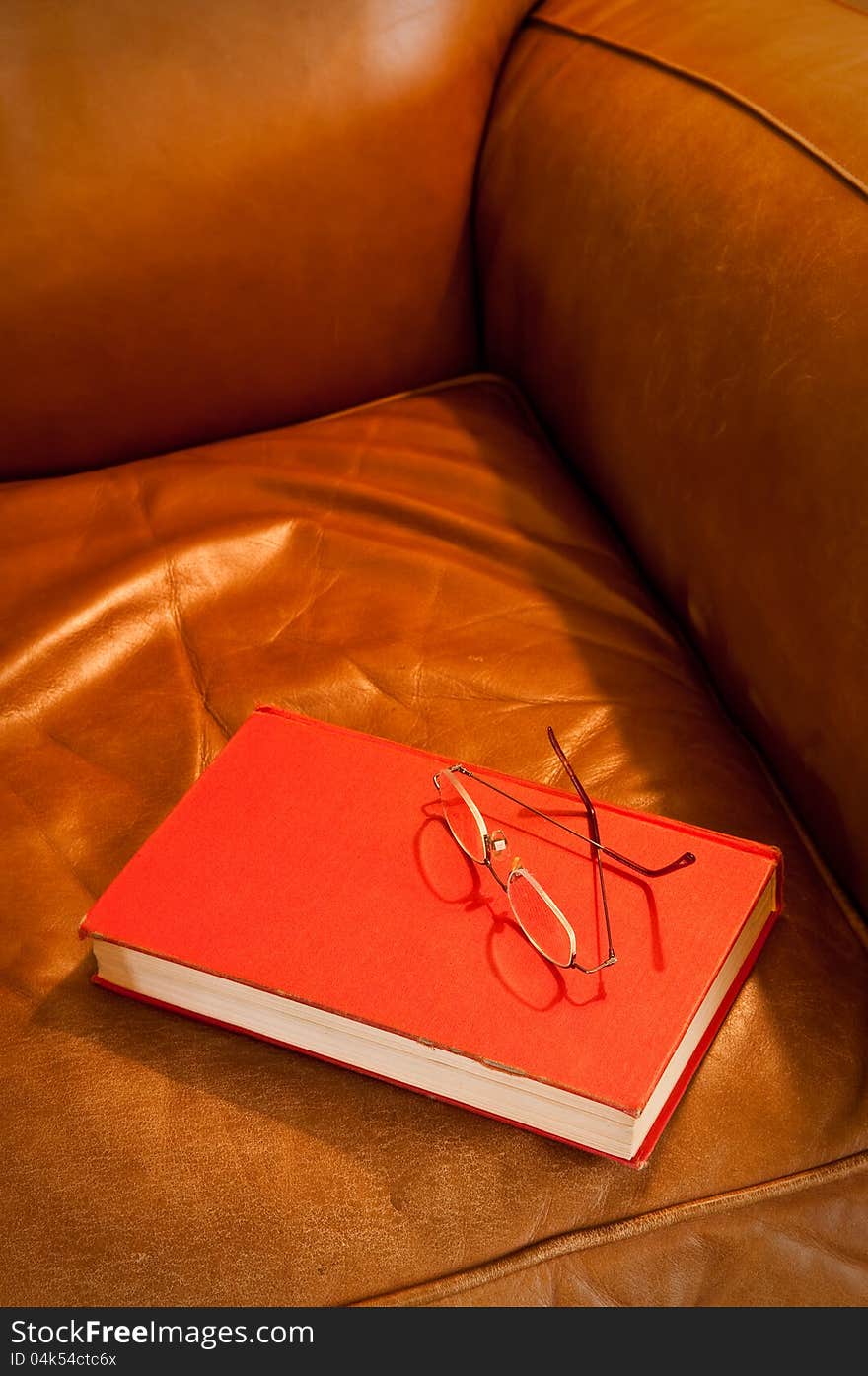 Comfy leather chair with red book and glasses, waiting for a reader. Comfy leather chair with red book and glasses, waiting for a reader