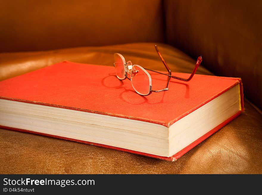 Comfy leather chair with red book and glasses, waiting for a reader. Comfy leather chair with red book and glasses, waiting for a reader