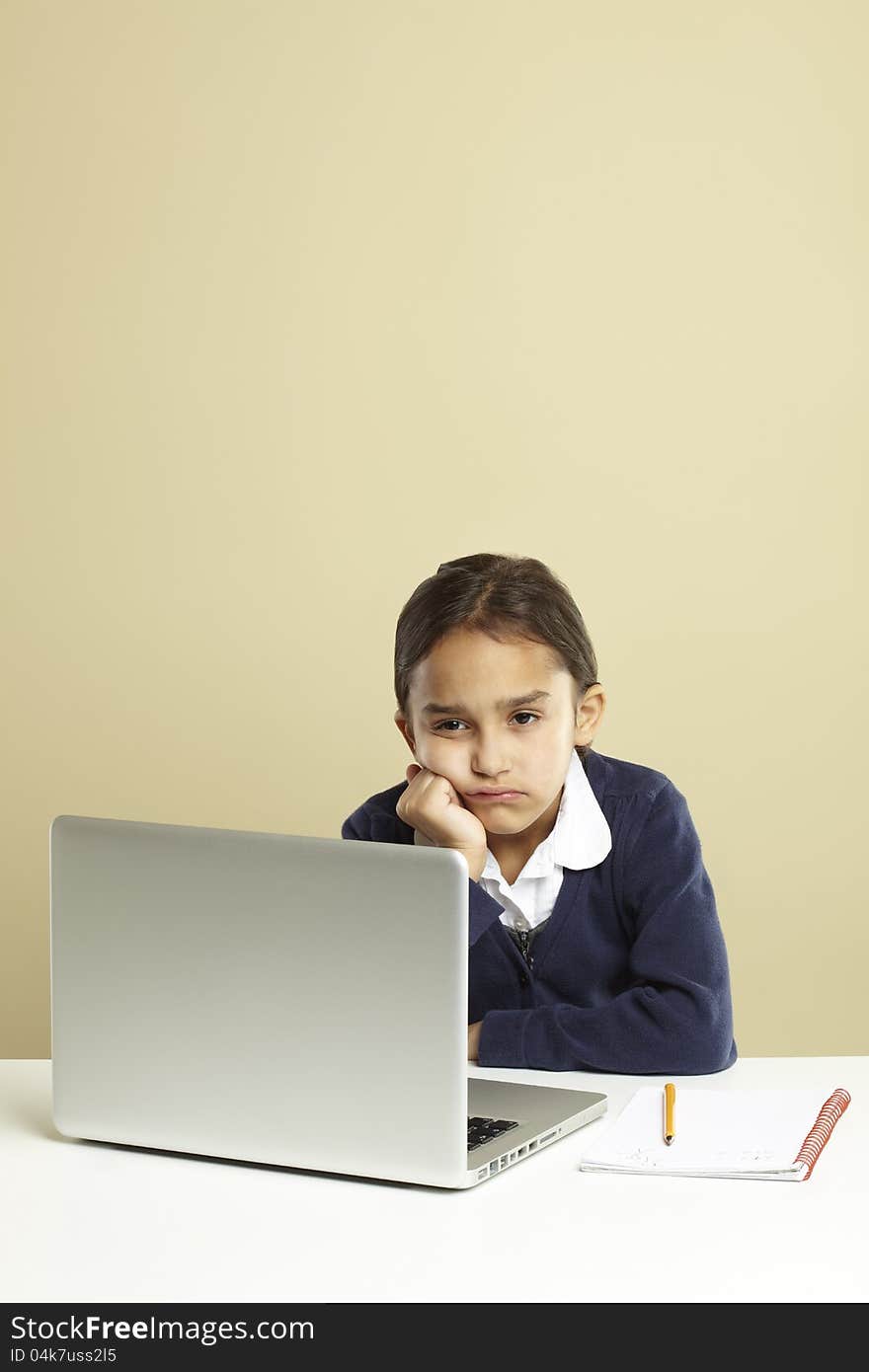 Young girl using laptop on white desk with homework looking bored