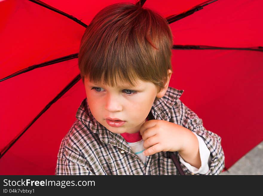 Little boy with a red umbrella in his hand is listening to the rain. His face collected. Little boy with a red umbrella in his hand is listening to the rain. His face collected.