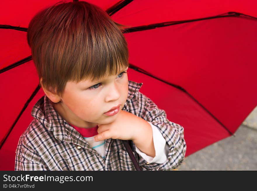 Little boy with a red umbrella in his hand is listening to the rain. His face collected. Little boy with a red umbrella in his hand is listening to the rain. His face collected.