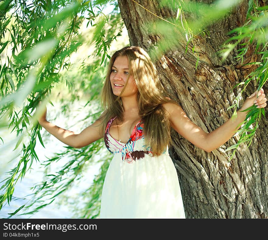 Beautiful young woman standing under the branches of willow tree. Beautiful young woman standing under the branches of willow tree