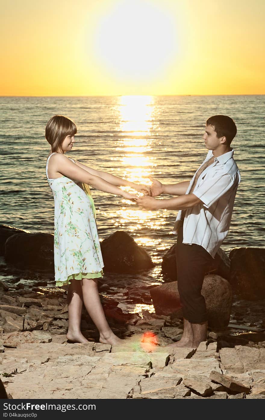 Young couple staying on stones near the lake at sunset. Young couple staying on stones near the lake at sunset