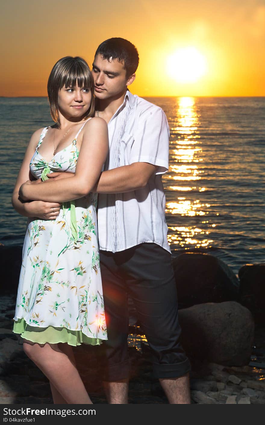 Young couple staying on stones near the lake at sunset. Young couple staying on stones near the lake at sunset