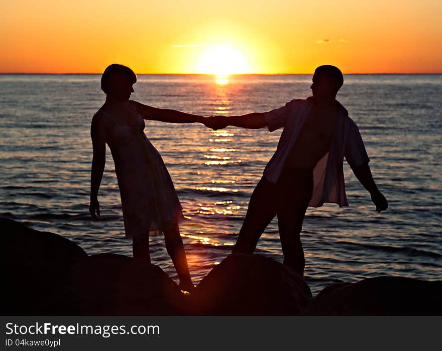 Young couple staying on stones near the lake at sunset. Young couple staying on stones near the lake at sunset