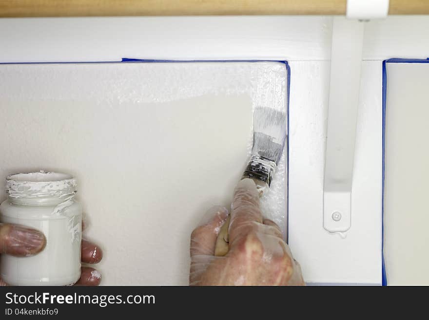 Hand holding a glass jar of white paint in left hand while painting a corner of a wall under a shelf in a closet close up. Hand holding a glass jar of white paint in left hand while painting a corner of a wall under a shelf in a closet close up.