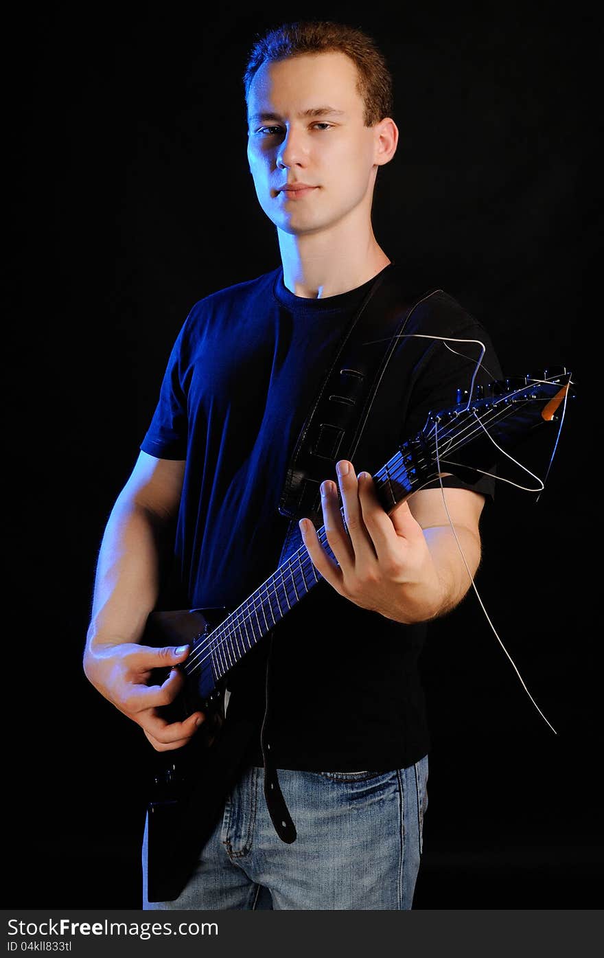 A young guy with an electric guitar on a black background. A young guy with an electric guitar on a black background